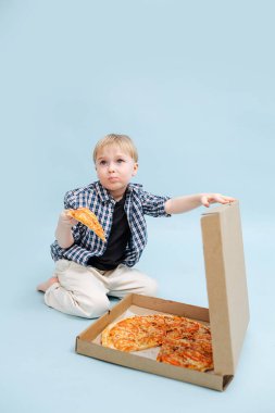 Squimish sarışın çocuk elinde pizza dilimiyle yerde oturuyor, kutu kapağını tutuyor.