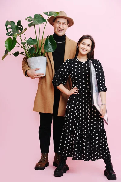 Retrato de una pareja joven única. Hombre sosteniendo una planta, mujer sosteniendo una pintura —  Fotos de Stock