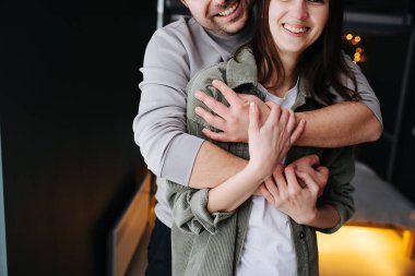 Mutlu bir çiftin kırpılmış görüntüsü. Adam kadına arkadan sarılıyor. Kapat, yarım yüz, bulanık arkaplan.