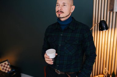 Ciddi bir orta yaşlı adam elinde fincanla evde sıcak bir içki içiyor. Zarif ince sakalı ve bıyığı var..