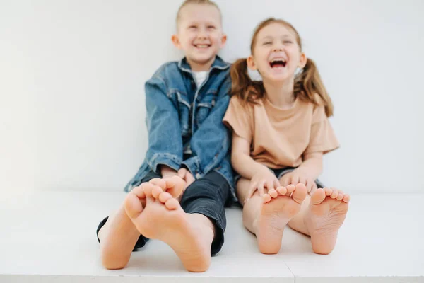 Glada syskon som sitter på ett bord med bara fötter. Båda skrattar. — Stockfoto