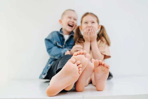 Skrattande syskon sitter på ett bord med bara fötter. Båda skrattar högt. — Stockfoto