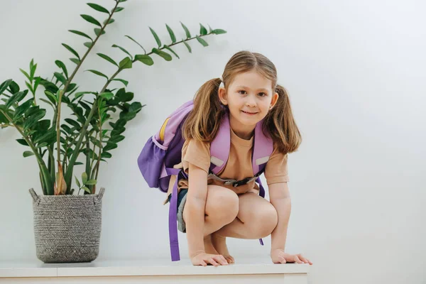 可爱可爱的小女孩 两条马尾辫 白色的桌子 背着紫色的背包 她已经准备好上学了 白色背景 — 图库照片
