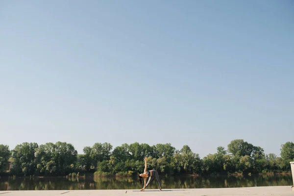Nehir kenarındaki kaldırımda yoga yapan bir kadının görüntüsü. — Stok fotoğraf