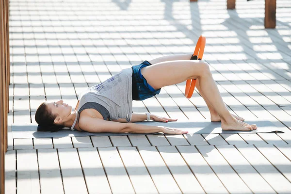 Hardwerkende vrouw doet oefeningen, brug poseren met een hoepel tussen haar knieën — Stockfoto