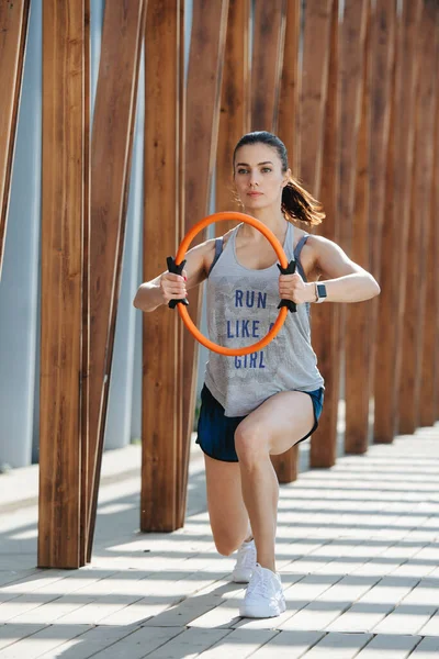 Atletische brunette doen pilates oefening met een hoepel onder houten frame — Stockfoto