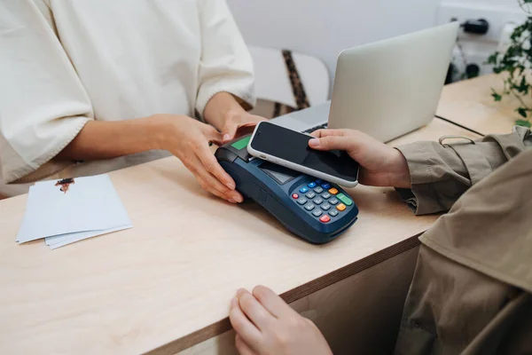 Woman paying with her phone on a cash terminal. Hands only. Seller holding it with both hands.