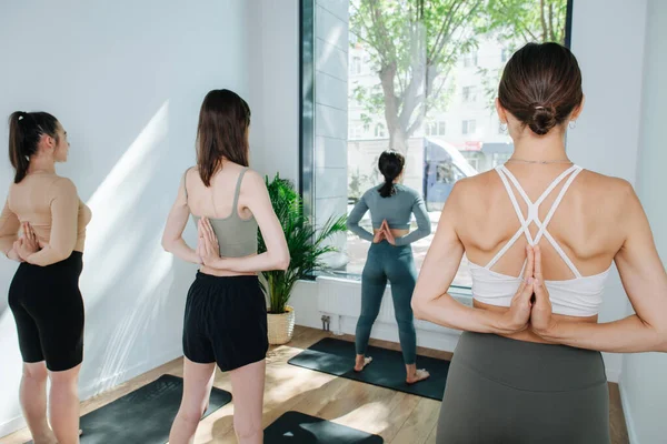 Trío de mujeres practicando yoga delante de un instructor, uniendo las manos detrás —  Fotos de Stock