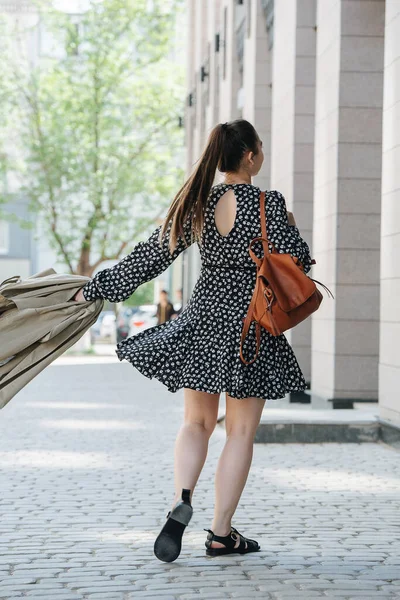女性は舗装された通りを歩いて 彼女のコートを振って気をつけてください 花模様の夏のミニドレスを着てる — ストック写真