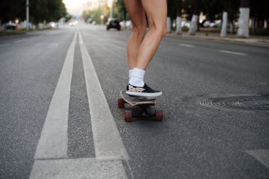 Sabahın erken saatlerinde boş bir şehir yolunda kaykay süren bir kadının bacakları. Mini şort yüzünden beyaz çorap, spor ayakkabı ve çıplak bacak giyiyor..