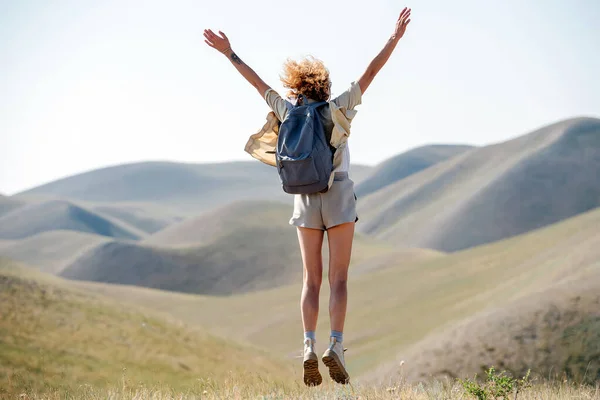 一个快乐的女人在美丽的山景中跳着 把双手抛向空中 从后面 — 图库照片