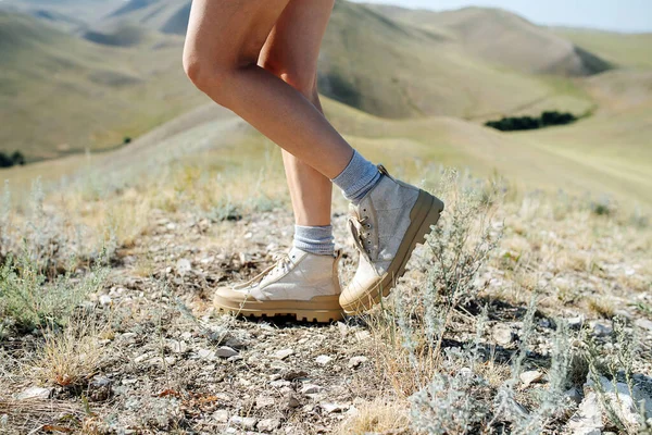 Çimenli bir çimlerin üzerinde duran ve tepe manzarasından zevk alan bir kadının kırpılmış görüntüsü. Kafası yok. Bir bacağını kaldır, dizine doğru eğil..