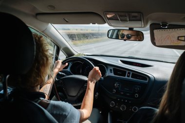 Yüksek açılı arka koltuk manzaralı bir kadın arabasını kullanıyor. Yüksek açı. Güneş gözlüğü takıyor, yüzü aynaya yansıyor..