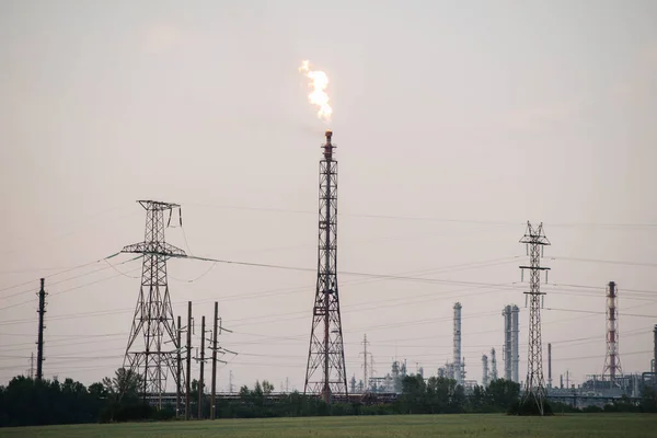 Industrial zone. Gas flare and high voltage electric lines over grey sky. Low angle.