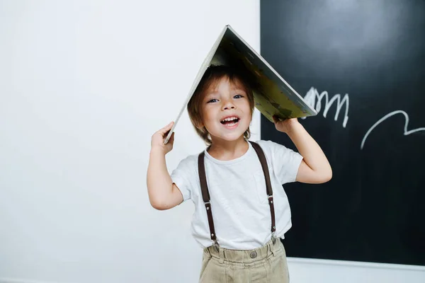 Niño Juguetón Posando Para Una Foto Llevando Libro Abierto Cabeza — Foto de Stock