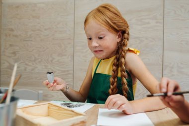 Küçük komik kızıl kız suluboya parmak izi yapıyor. Düşük açı.