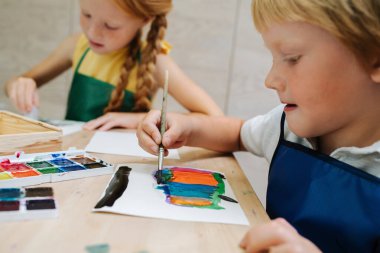 Suya batmış çocuklar suluboya boyayla resim yapıyor. Düşük açı.