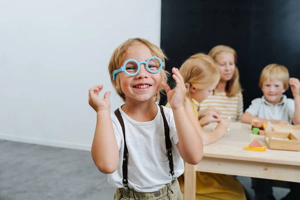 Маленький мальчик играет в голубые пластиковые игрушечные очки, блестяще улыбаясь. — стоковое фото