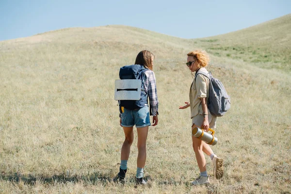 女性の友達と芝生の丘で 立って 何かについて議論ハイキング話している 乾燥した草で覆われた斜面の真ん中で停止します — ストック写真