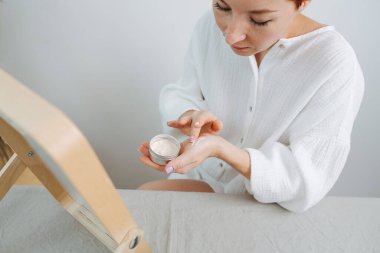 Dikkat et, kısa saçlı kadın cilt reaksiyonuna bakarak kapatıcıyı bileğine takıyor. Çevre dostu ürünler falan kullanıyor. Aynanın önünde otururken.