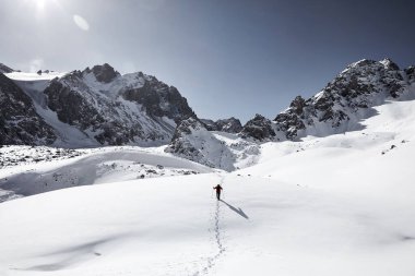 Sırt çantalı bir adam güzel dağlarda kar tepesinde yürüyor Almaty, Kazakistan 'daki mavi gökyüzüne karşı. 