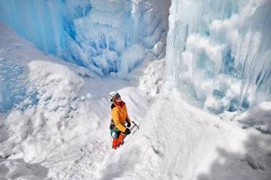 Almaty, Kazakistan 'daki dağlarda donmuş şelalenin yanında buzdan baltayla turuncu ceketli bir kadın tırmanıyor.