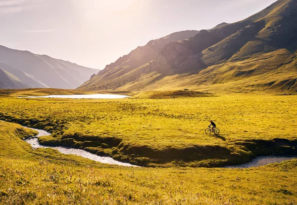 Man on mountain bike rides near the lake at the green mountain valley at sunrise. Recreation, travel and healthy lifestyle concept.