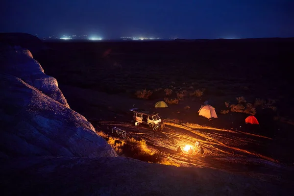 カザフスタンの夜の空の下でバンや自転車の近くの砂漠の峡谷でキャンプでたき火の近くの人々のシルエット — ストック写真