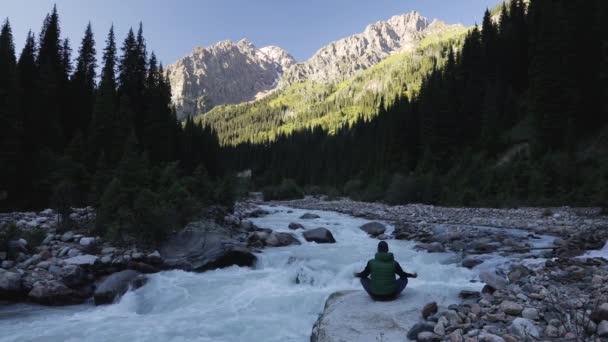 Мужчина в медитации позирует у реки на горе — стоковое видео