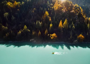 Adam sonbahar zamanı dağ gölünde sarı sal üzerinde kürek çekiyor. Hava Aracı Çekimi.