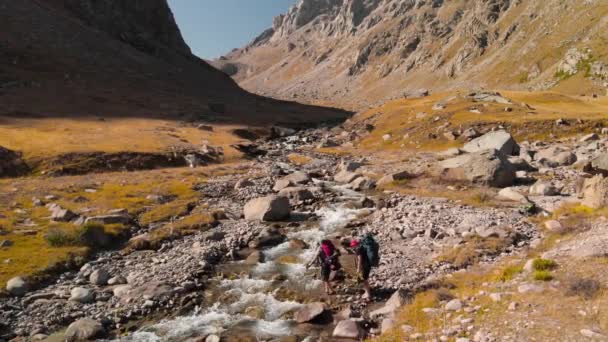 Caminhantes cruzando o rio nas montanhas tiro aéreo — Vídeo de Stock