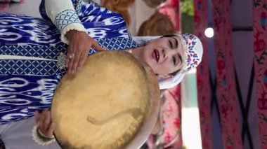 Semerkant, UZBEKISTAN - 23 Mayıs 2025: Geleneksel tef oyunları takan ve antik Semerkant kentinde düzenlenen bir halk etkinliği sırasında Registan meydanında şarkı söyleyen Özbek müzisyenler dikey video grubu