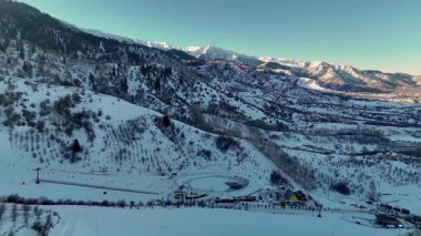 Oi Qaragai kayak merkezi Kazakistan 'daki bakir beyaz kar ve çam ağacı ormanlarıyla kaplı dağ vadisi manzarasının insansız hava aracı görüntüsü.