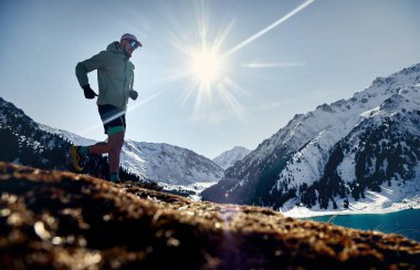 Kış güneşli bir günde dağ vadisinde siluette koşan erkek atlet. Spor giysileriyle doğada koşmak.