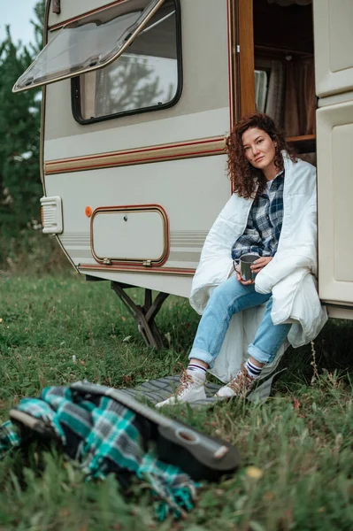 Fille assise sur l'échelle du camping-car avec une tasse dans les mains enveloppé dans une couverture — Photo
