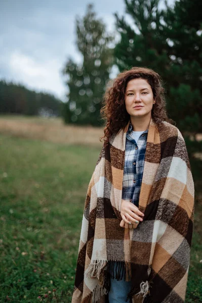 Aantrekkelijk meisje verpakt in een geruite ruit op een bos en veld achtergrond — Stockfoto