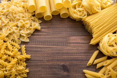 Ahşap arka planda farklı türde makarna. Farfalle, fettuccine, noodle, fusilli ve penne rigate..