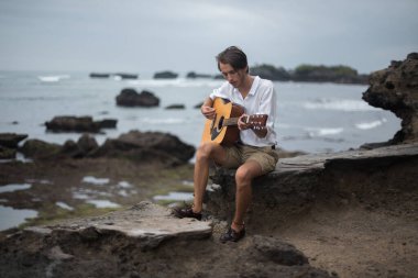 Gitarla suyun önünde duran bir adam.