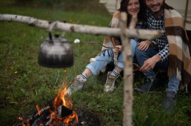 Kareli ekoseli bir çift, karavanın yanında lokum pişiriyor..