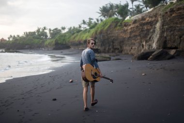 Sahilde gitar çalan romantik bir genç adam.