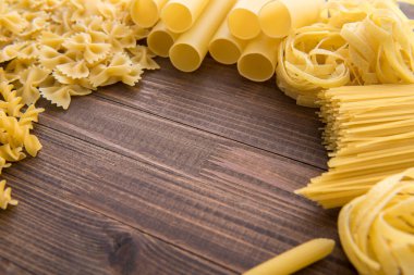 Ahşap arka planda farklı türde makarna. Farfalle, fettuccine, noodle, fusilli ve penne rigate..
