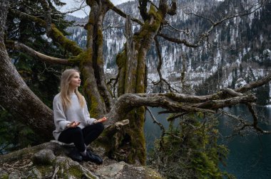 Kız ağaçta oturur ve mavi göl arka planında meditasyon yapar. Abhazya 'daki Ritsa Gölü