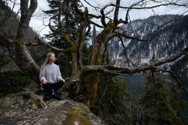 Kız ağaçta oturur ve mavi göl arka planında meditasyon yapar. Abhazya 'daki Ritsa Gölü