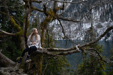 Kız ağaçta oturur ve mavi göl arka planında meditasyon yapar. Abhazya 'daki Ritsa Gölü
