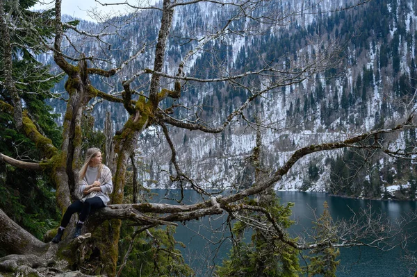 Kız ağaçta oturur ve mavi göl arka planında meditasyon yapar. Abhazya 'daki Ritsa Gölü