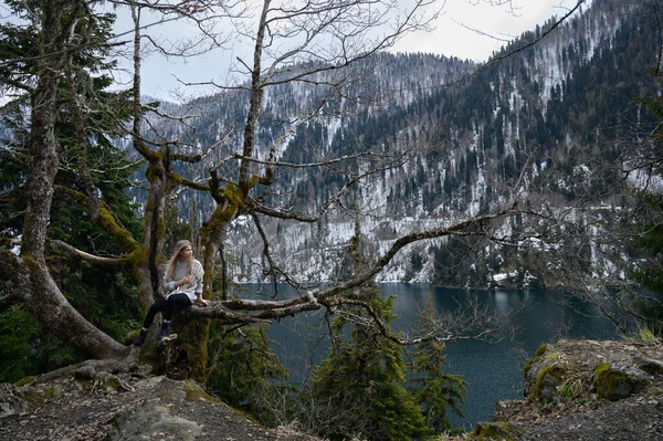Kız ağaçta oturur ve mavi göl arka planında meditasyon yapar. Abhazya 'daki Ritsa Gölü
