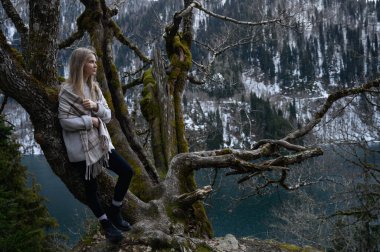 Kız ağaçta oturur ve mavi göl arka planında meditasyon yapar. Abhazya 'daki Ritsa Gölü