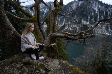 Kız ağaçta oturur ve mavi göl arka planında meditasyon yapar. Abhazya 'daki Ritsa Gölü