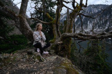 Kız ağaçta oturur ve mavi göl arka planında meditasyon yapar. Abhazya 'daki Ritsa Gölü