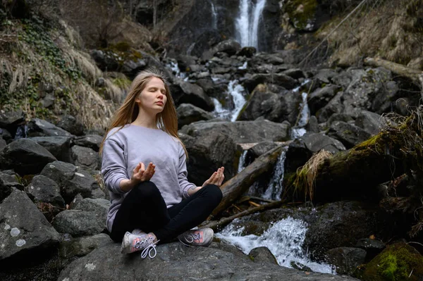 Menina senta-se em uma árvore e medita perto do rio da montanha na Abcásia — Fotografia de Stock